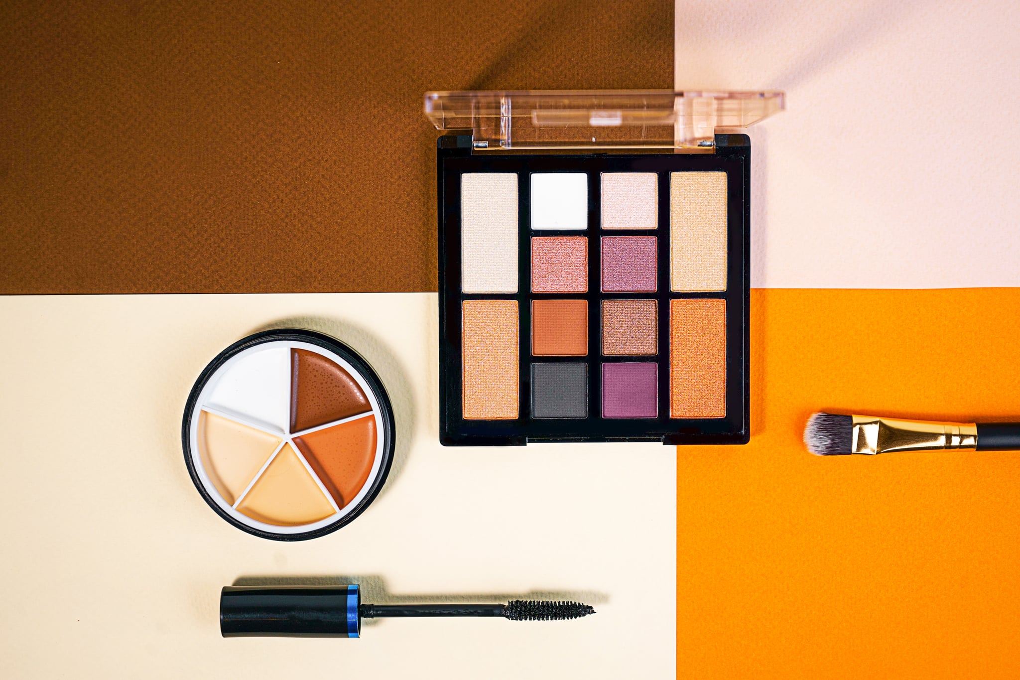 Set of beauty products laid out on a colourful background. Decorative cosmetics and makeup brushes on a pink, brown, beige and orange background, top view. Copy space.