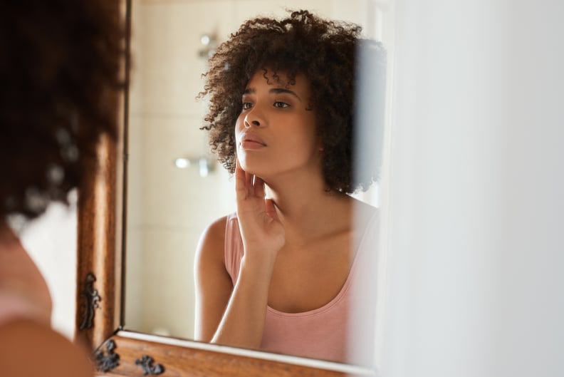 Young woman examining her skin in the bathroom mirror.