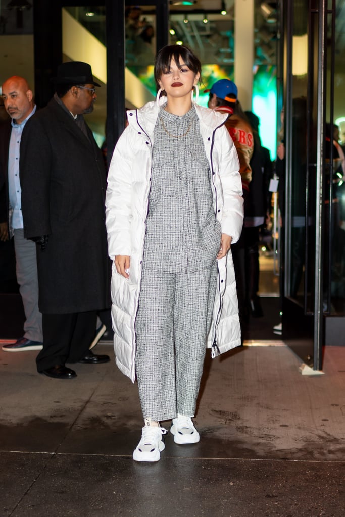 Selena Gomez can perform a style switch-up at the drop of a hat. Just a day after appearing on The Tonight Show in a retro Miu Miu dress, the "Look At Her Now" singer stepped out in NYC wearing its polar opposite: a houndstooth Totême set with a white full-length puffer coat from Everlane. Is anyone else getting major Billie Eilish vibes from this outfit? Selena showed off the ensemble for a meet and greet to promote her newly-released album at a Puma pop-up shop, and she looked fierce. 
Selena paired the bold matching set with Puma sneakers and oversized Fenty hoop earrings. Oh, did I forget to mention her stylist Kate Young threw a Cartier chain on their too? It's rumored to be above $7,000. That must definitely make Selena feel rare! Ahead, see more photos of Selena's look from her night out in NYC.