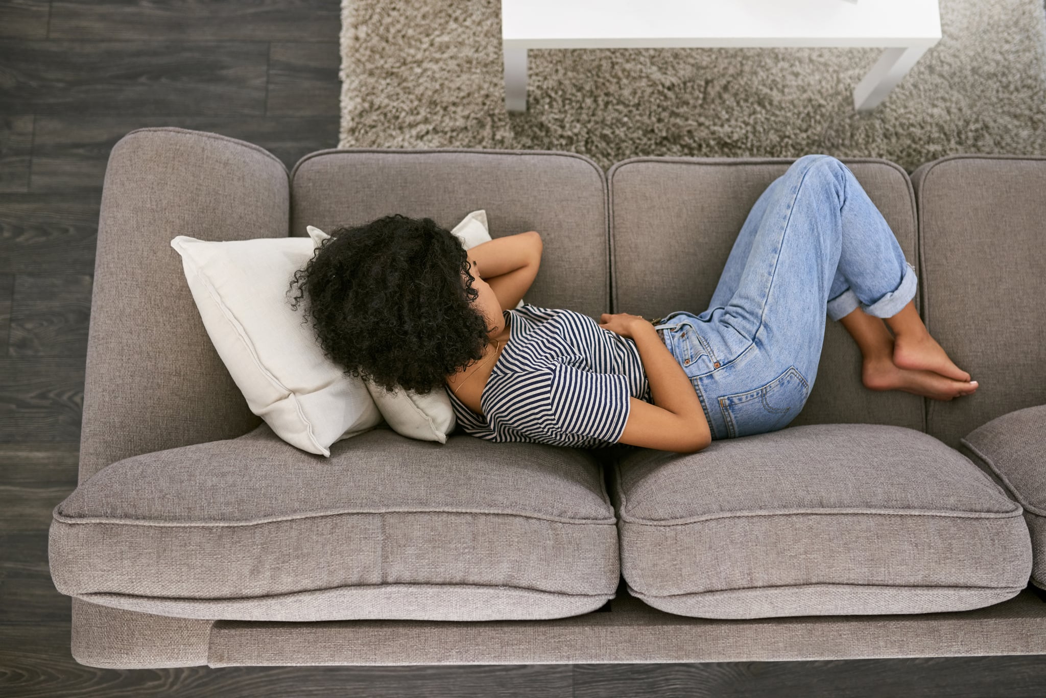 High angle shot of a young woman experiencing stomach pain on the sofa at home