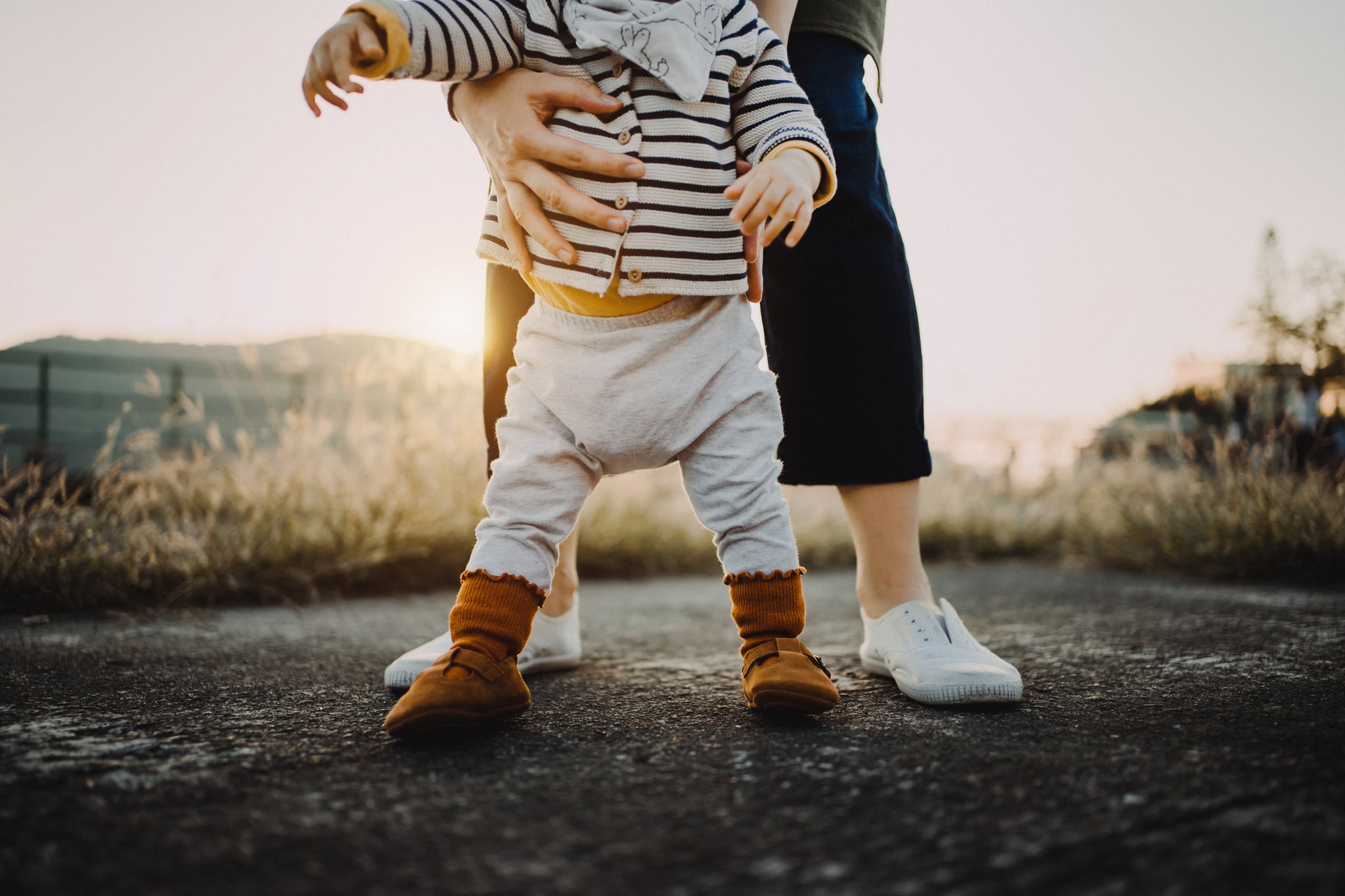 Mother holding baby daughter's body helping her to take her first step in life