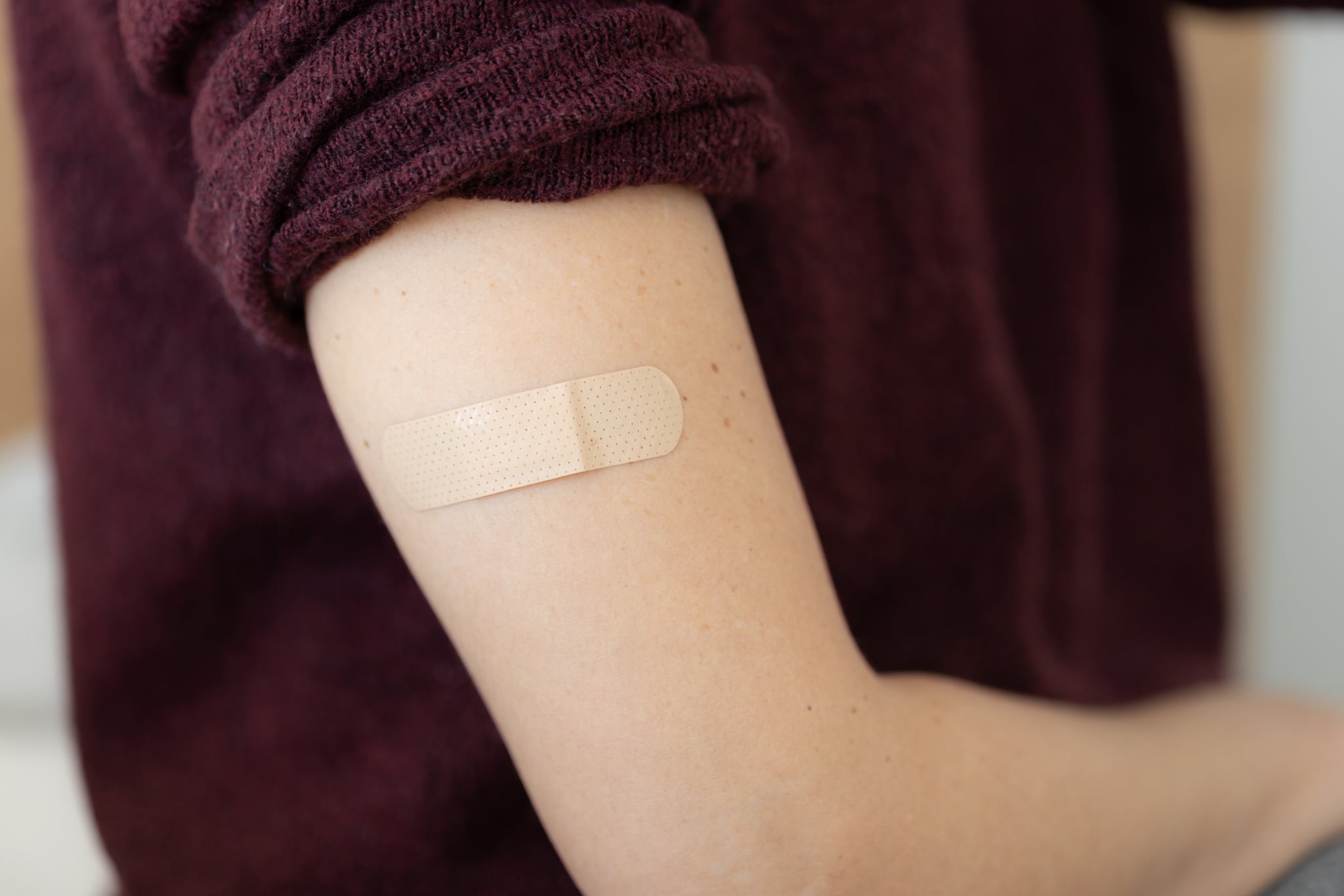 Close-up of a female patient young woman adhesive bandage to her own arm after taking vaccine.