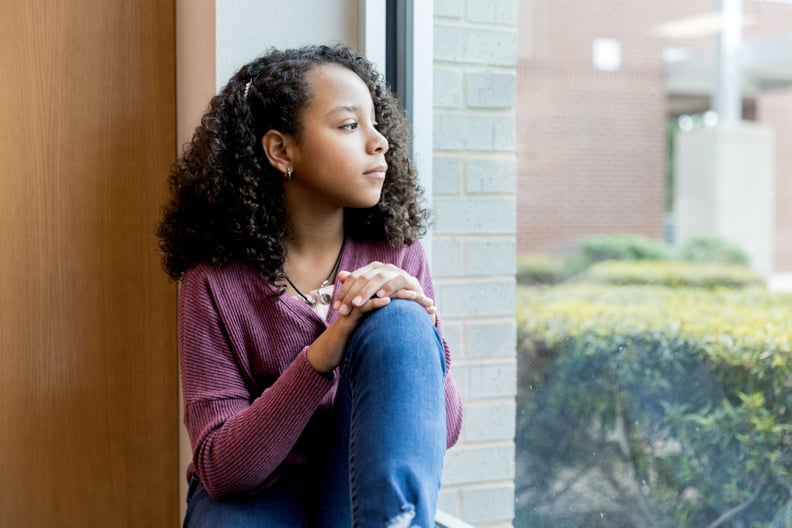 Lonely mixed race preteen schoolgirl day dreams as she looks through the window while at school.