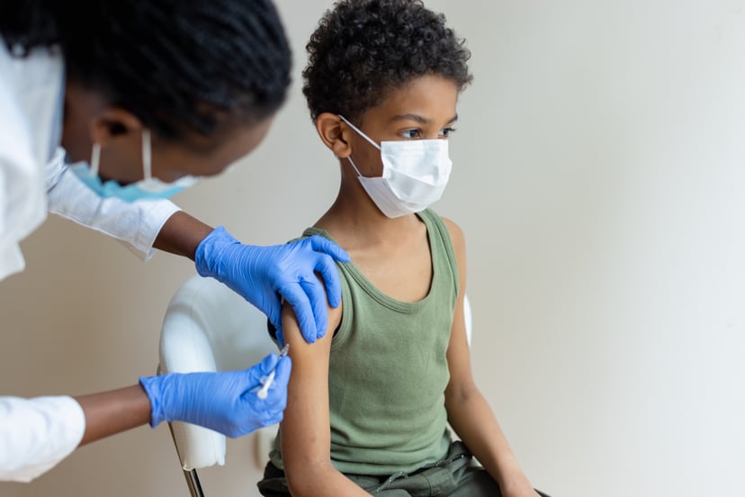 African-American, female injecting COVID-19 vaccine to a little black boy.  Shallow DOF, focus on a foreground
