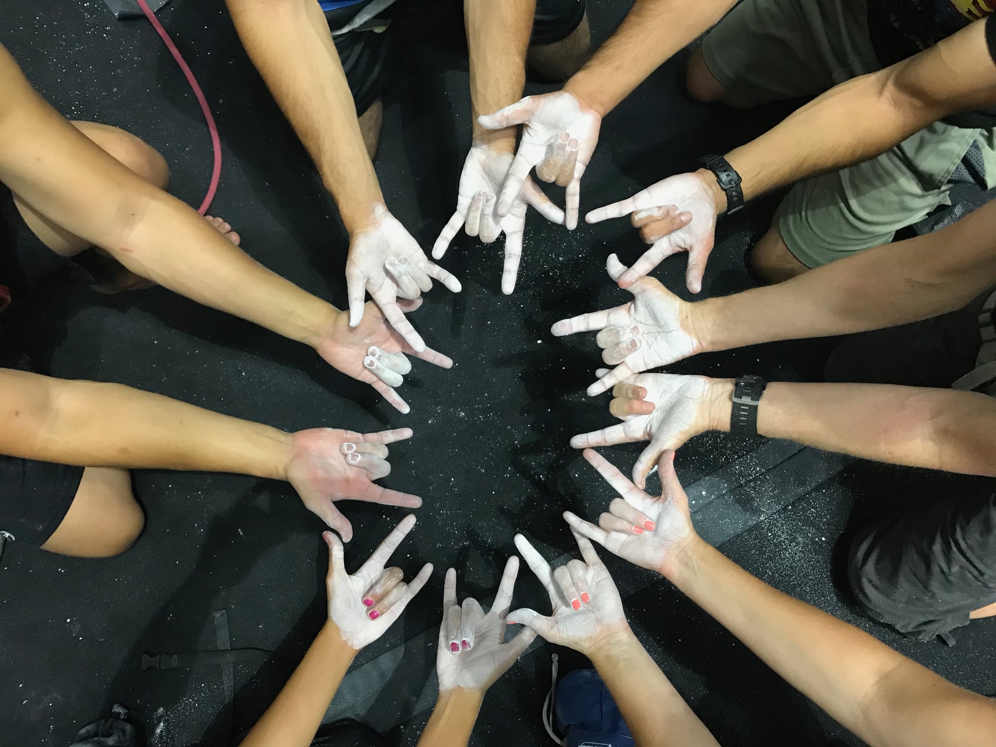 ASL Climbing Network members signing "I love you" in a circle with chalk-covered hands.
