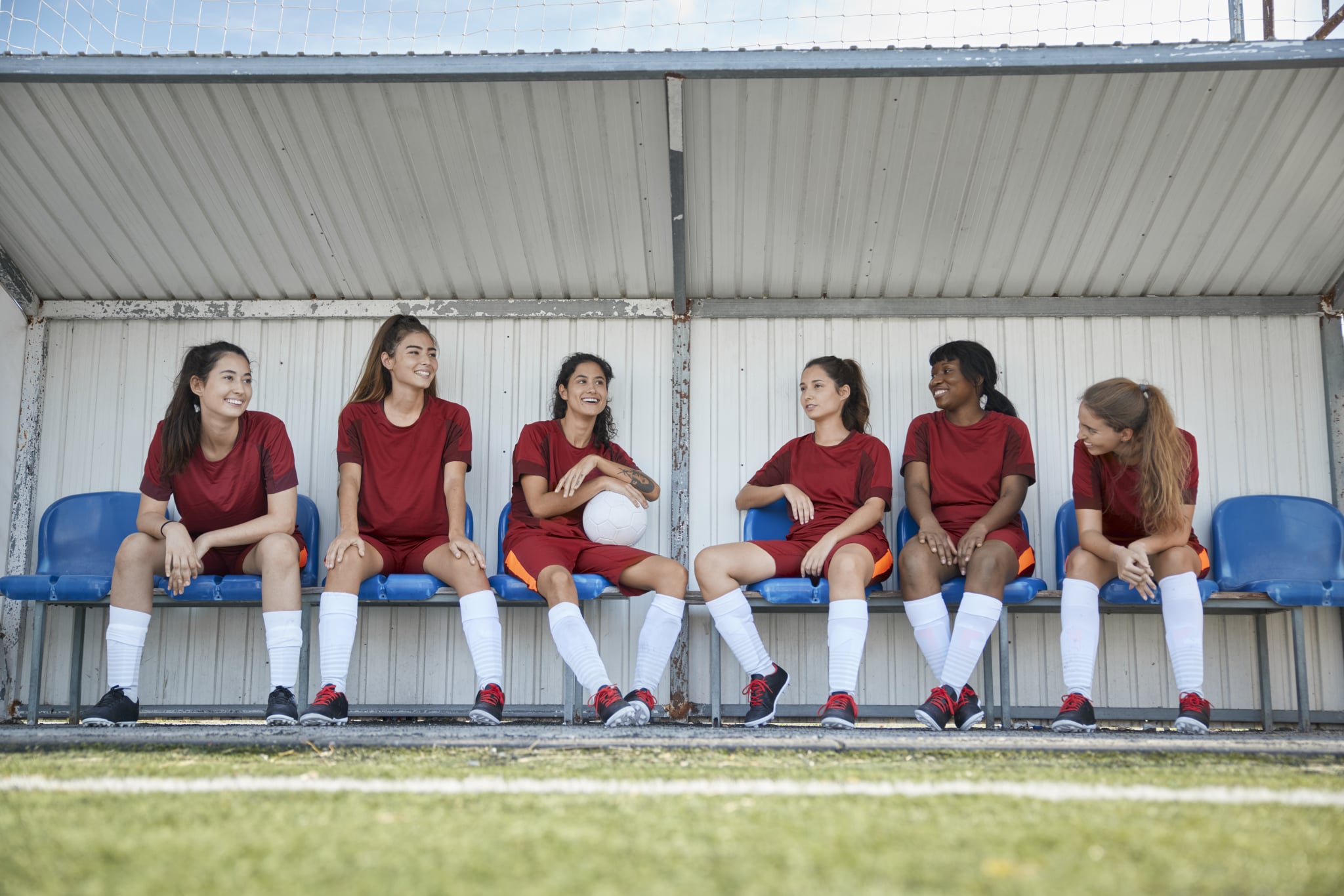 Group of multi-ethnic teenagers sitting on bench talking after soccer practice