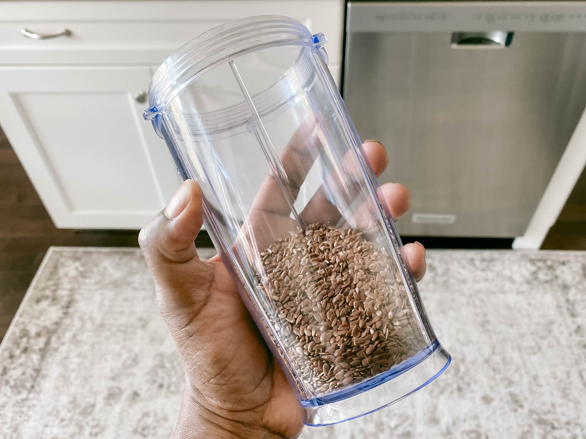 Close-up of woman's hand holding blender cup with whole flaxseed inside; which is healthier, chia or flaxseeds?