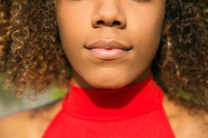 Lips and lower face of young African American woman. Closeup of black girl with pierced nose wearing casual red shirt. Healthy skin concept