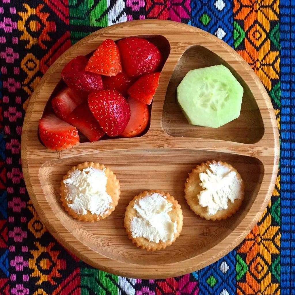 "Morning snack: crackers with cream cheese, strawberries, and a cucumber."