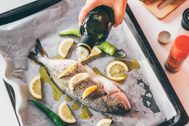 person pouring olive oil over Fish with herbs and lemon slices: how much fat do you need per day?