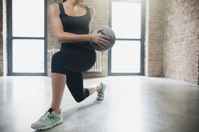 An unrecognizable young woman doing side lunges with medicine ball.