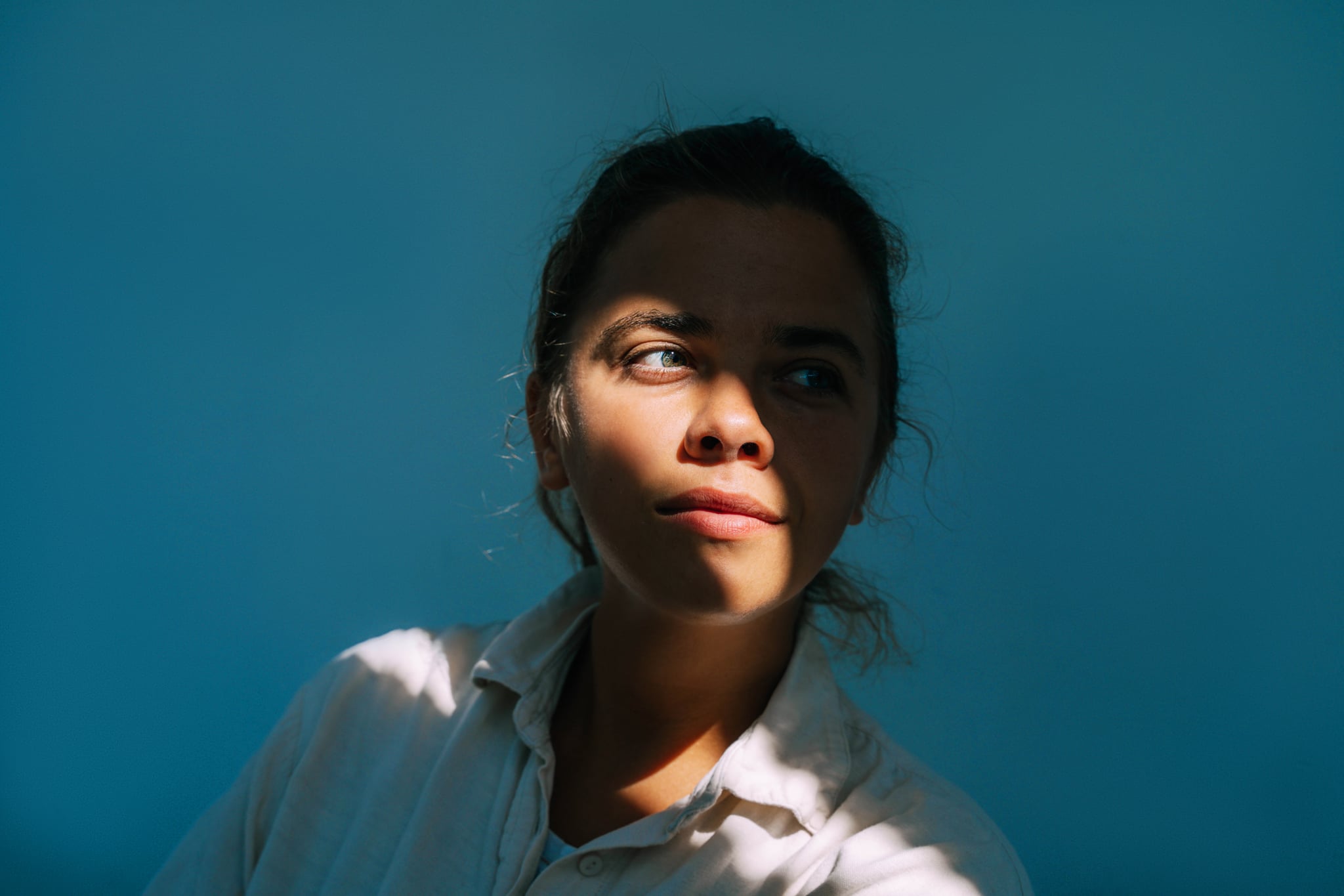 Portrait of beautiful woman on dark blue background with sun beam on face.