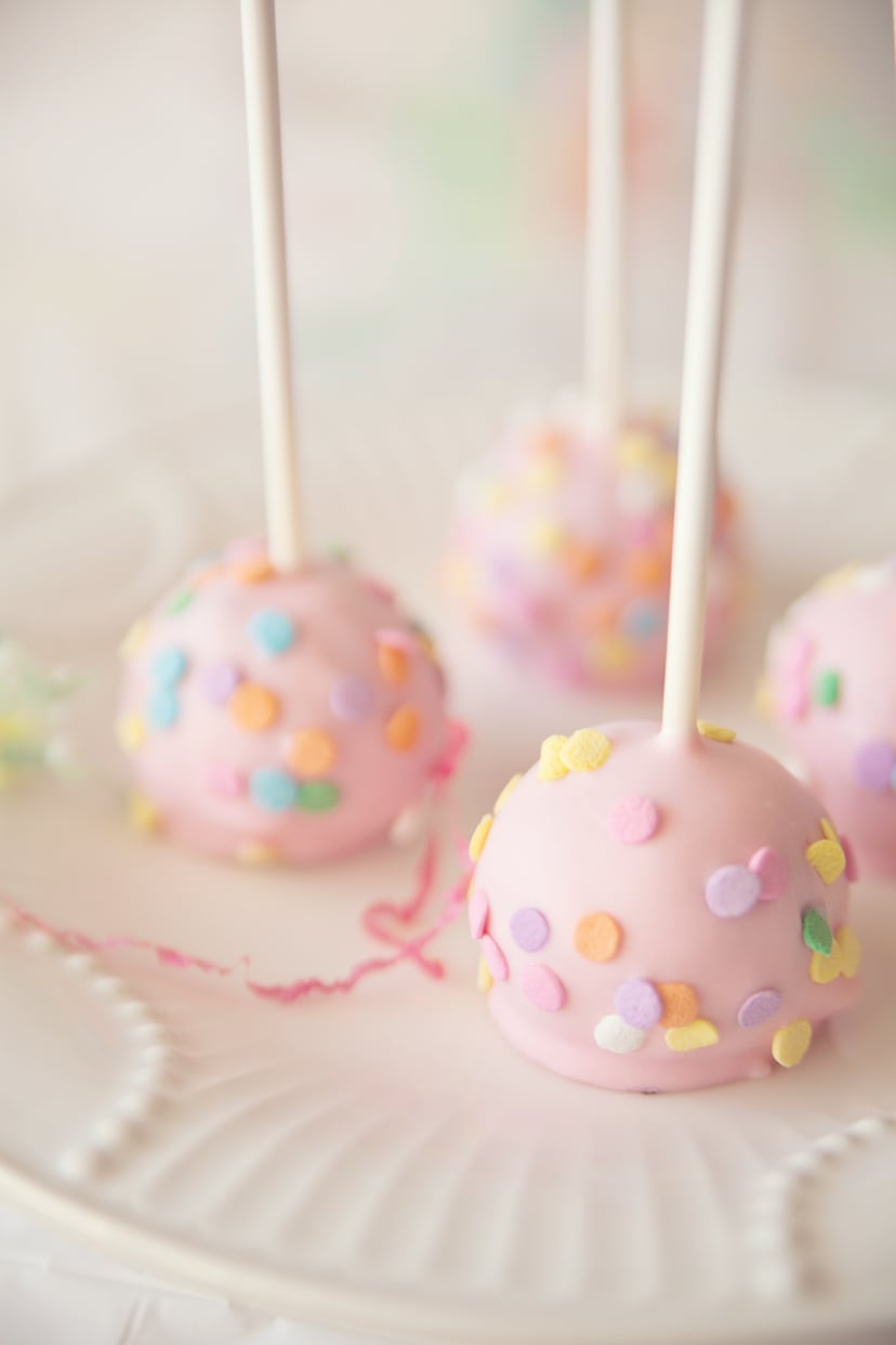 Some chocolate cake pops with pink candy coating and confetti sprinkles on plate.