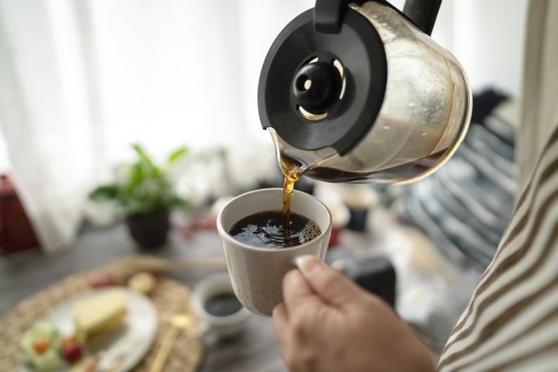 Young woman standing in front of window, pouring coffee at breakfast.