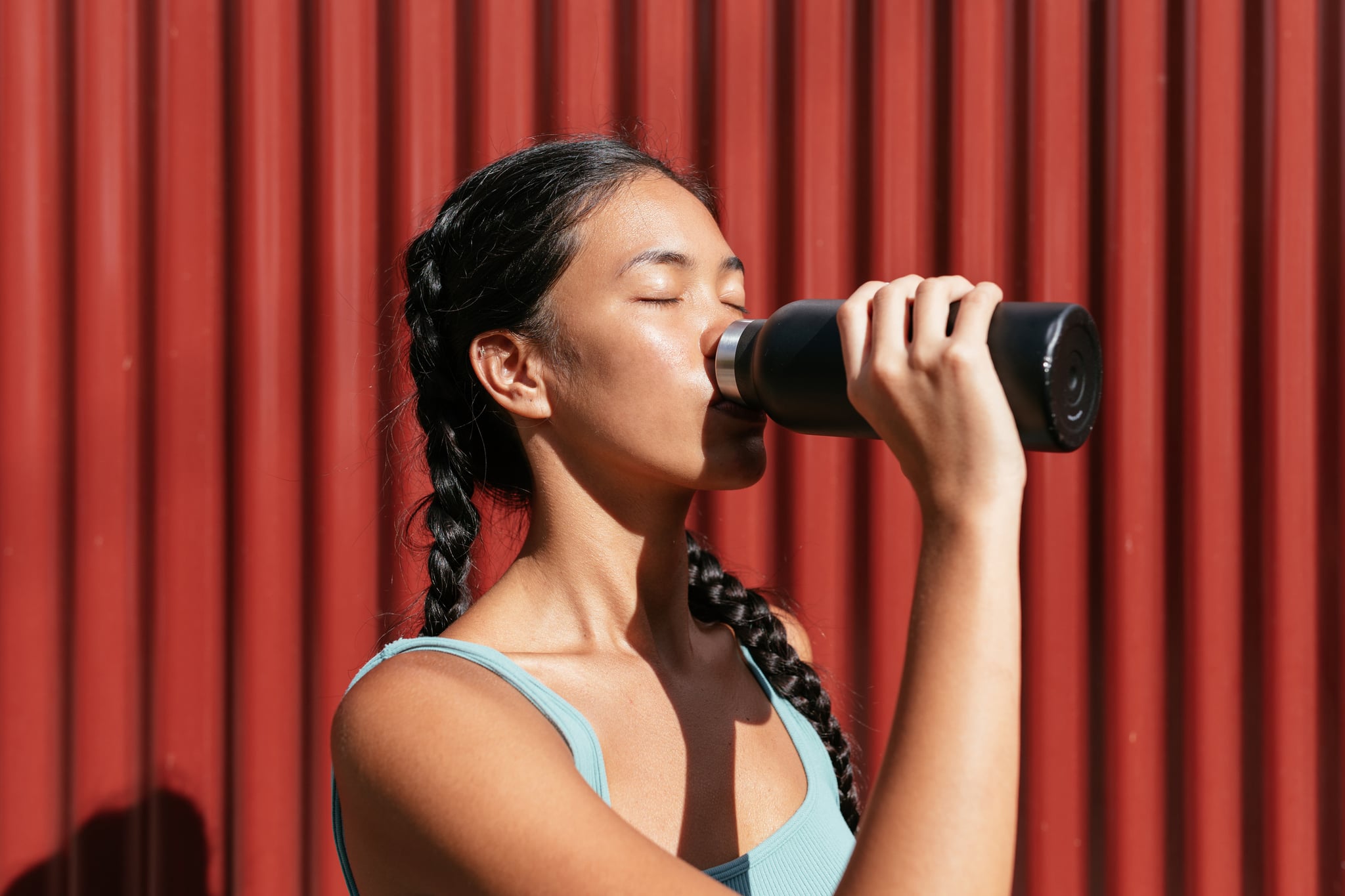 Woman with two braids drinking water in black aluminum bottle