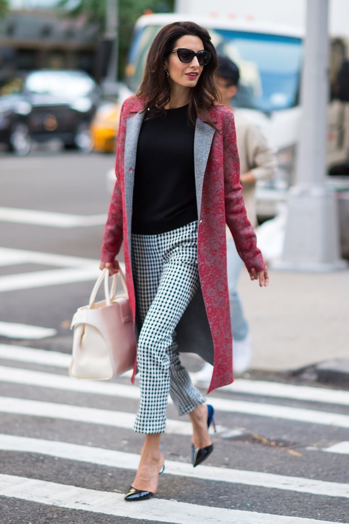 Amal mixed and matched patterns in her outfit while out and about in NYC in 2016. She wore a black sweater with a printed red coat, gingham-print trousers, and black pumps.