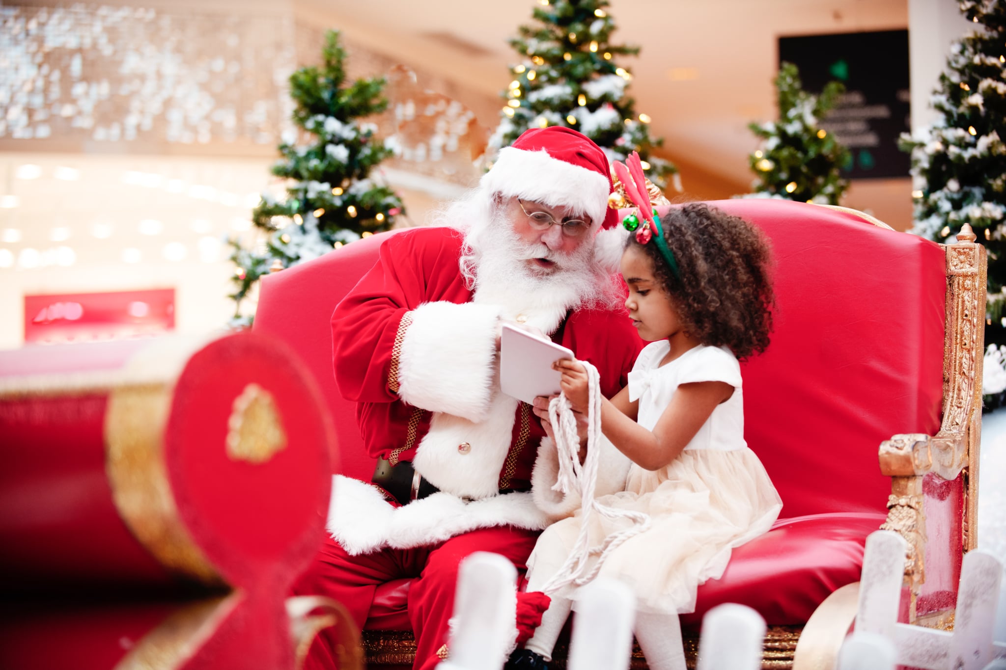 Multi-Ethnic family shops at Shopping Mall during Christmas Time with Santa Claus. Santa Claus and girl are shopping with digital tablet. Santa and girl is looking at the digital tablet. Santa Claus has a beautiful expression on his face. Photo was taken in Quebec Canada.