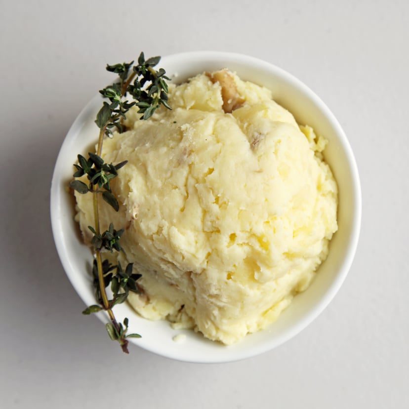 Bowl of mashed potatoes with sprig of herbs.