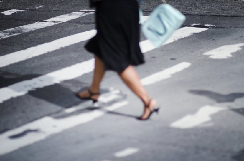 Defocused scene of a fashionable business woman in kitten heels rushing across a gritty city crosswalk (focus on the asphalt street in the background)