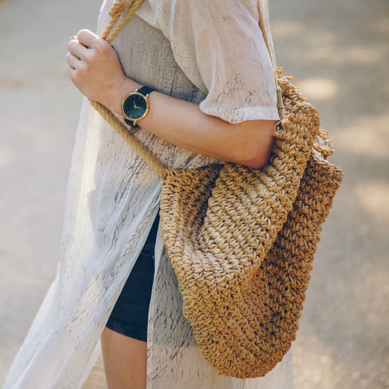 Close up of a stylish woman wearing a summer dress and holding a straw handbag while wearing a stylish wristwatch; Shutterstock ID 1243464847; Job: -