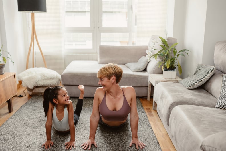 Cheerful latin mother and daughter doing yoga and looking to each other in a bright interior home. 