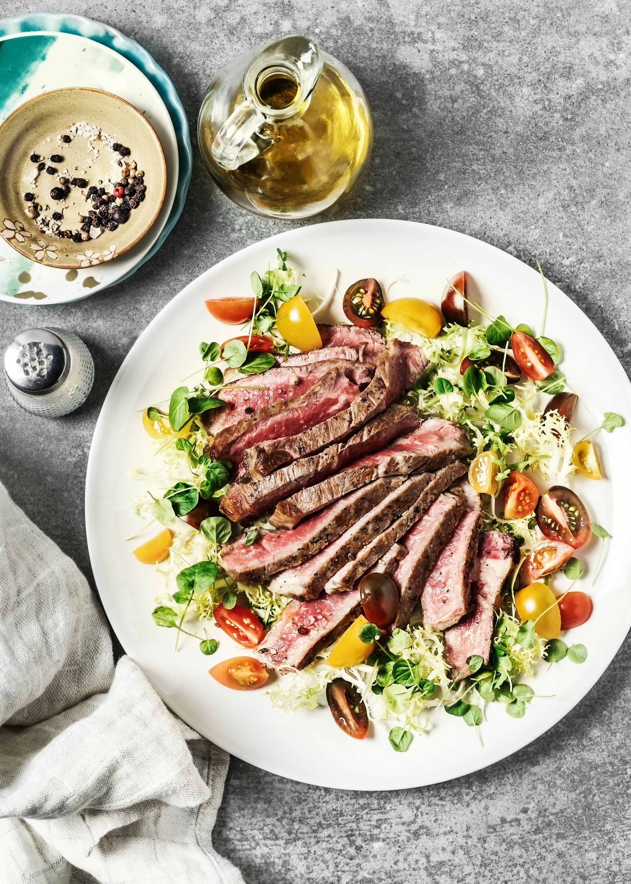 A plate of sliced steak with fresh salad on gray background