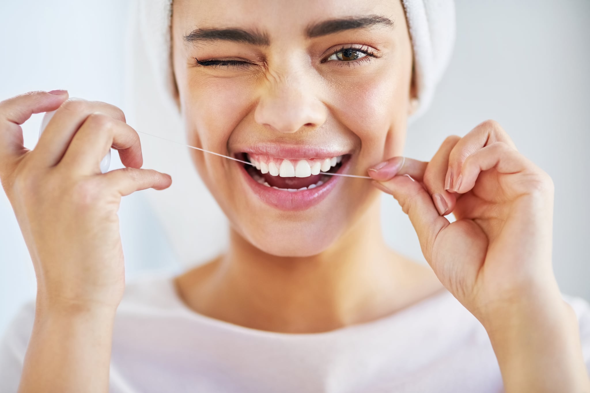 Portrait of a beautiful young woman flossing her teeth in the bathroom at home