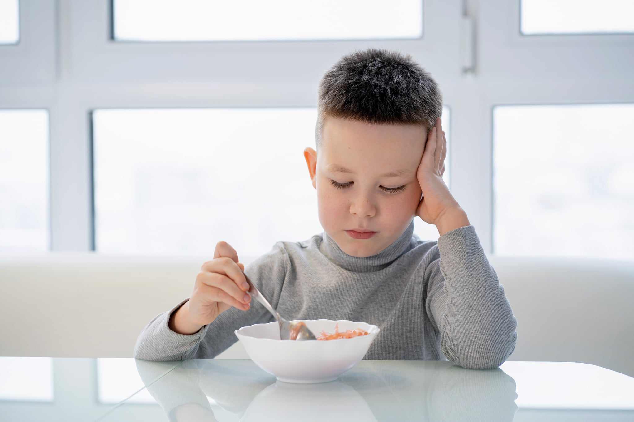 Little boy sits at the table and does not want to eat soup