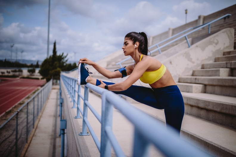 Woman listening to music and stretching her legs on sports track stadium stands after workout