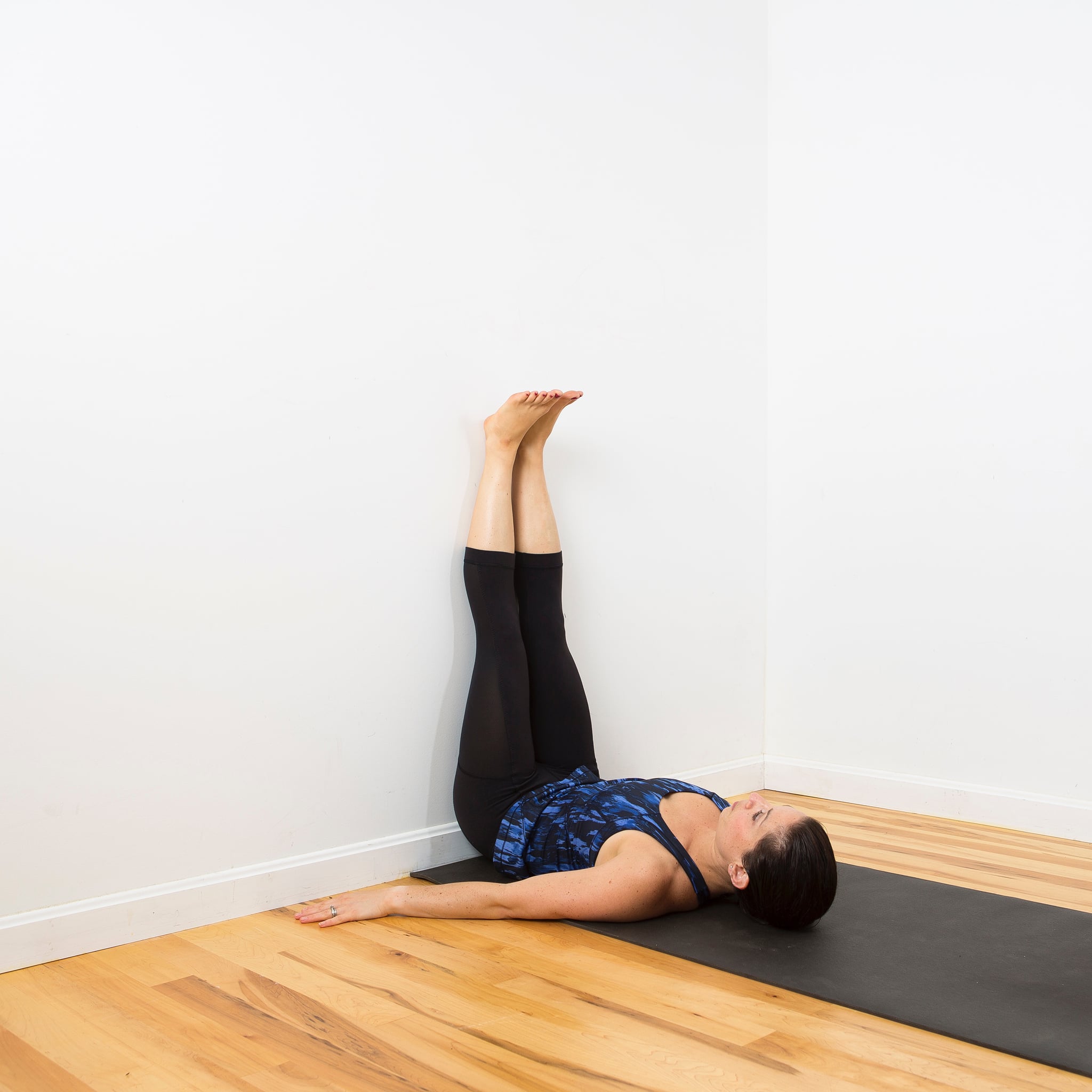 Person lying in legs up the wall pose against a white wall