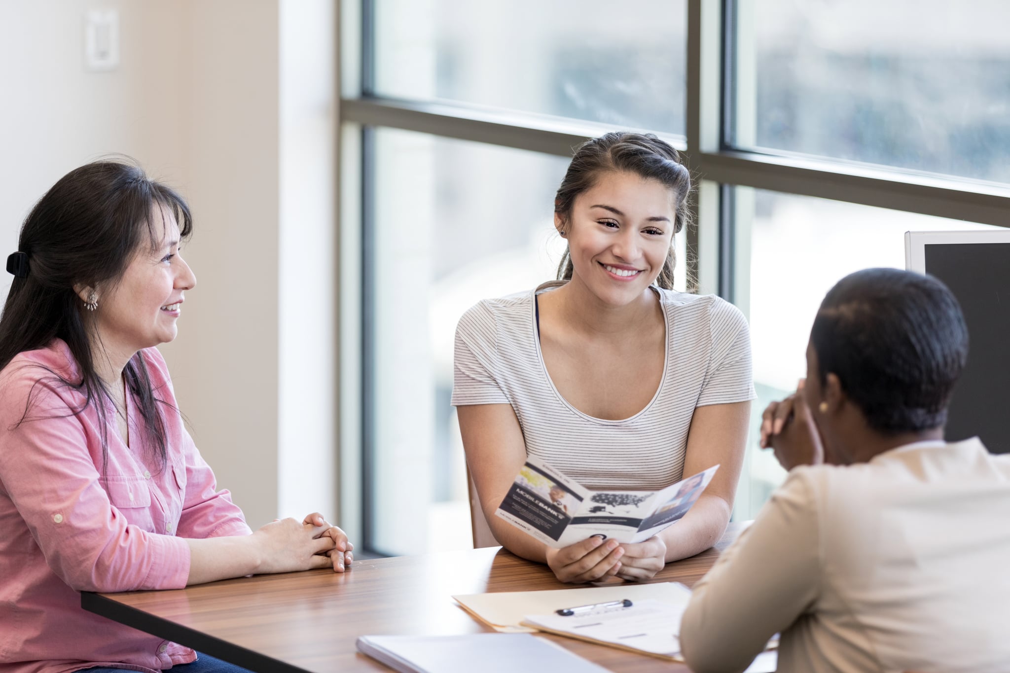 Young woman and her mother talk with a female bank employee about a student loan.