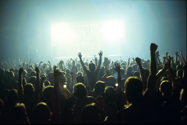 A general view of a rock concert taken from the back fo a venue showing the audience in silhouette raising their arms and cheering with bright lights shining from the stage, circa 1980. (Photo by Fin Costello/Redferns)