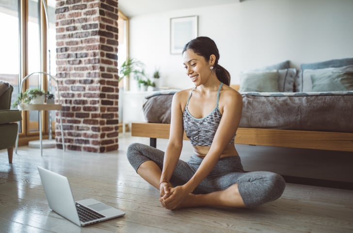 Young woman with a ponytail doing stretches while looking at a laptop screen