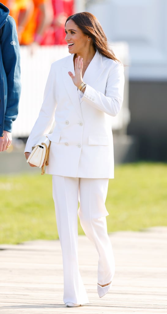 While attending the 2022 Invictus Games in the Netherlands, the Duchess of Sussex opted for all-white in a double-breasted pantsuit by Valentino, accessorised with a white purse and gold pendant necklace.