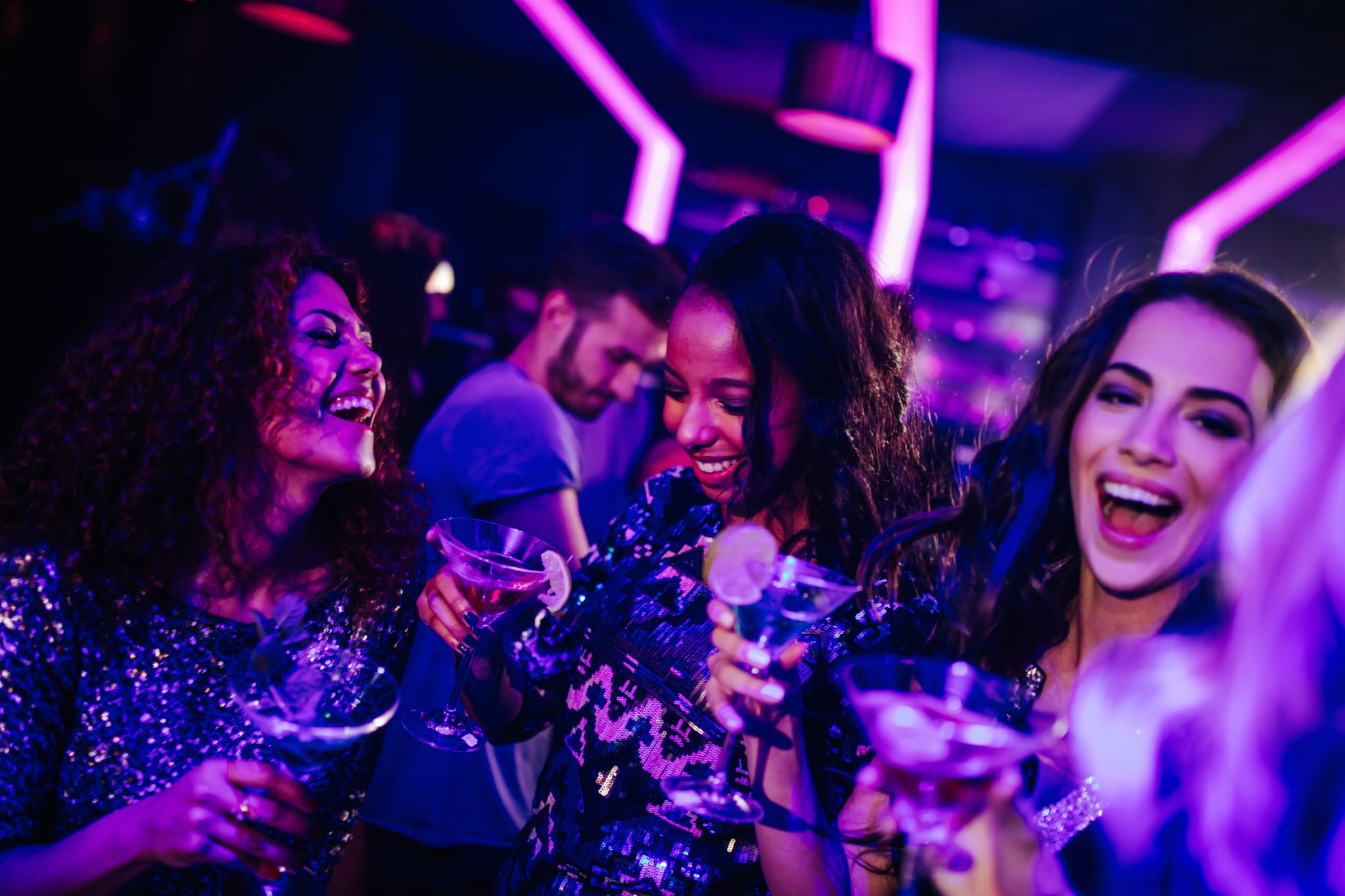 Three women are dancing at a night club and have drinks in their hands.