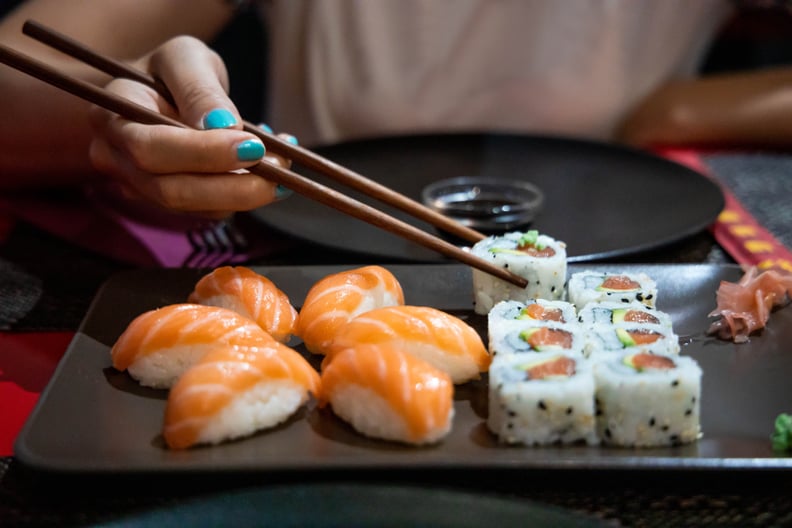 Woman with blue nails grabbing sushi off of black plate with chopsticks.