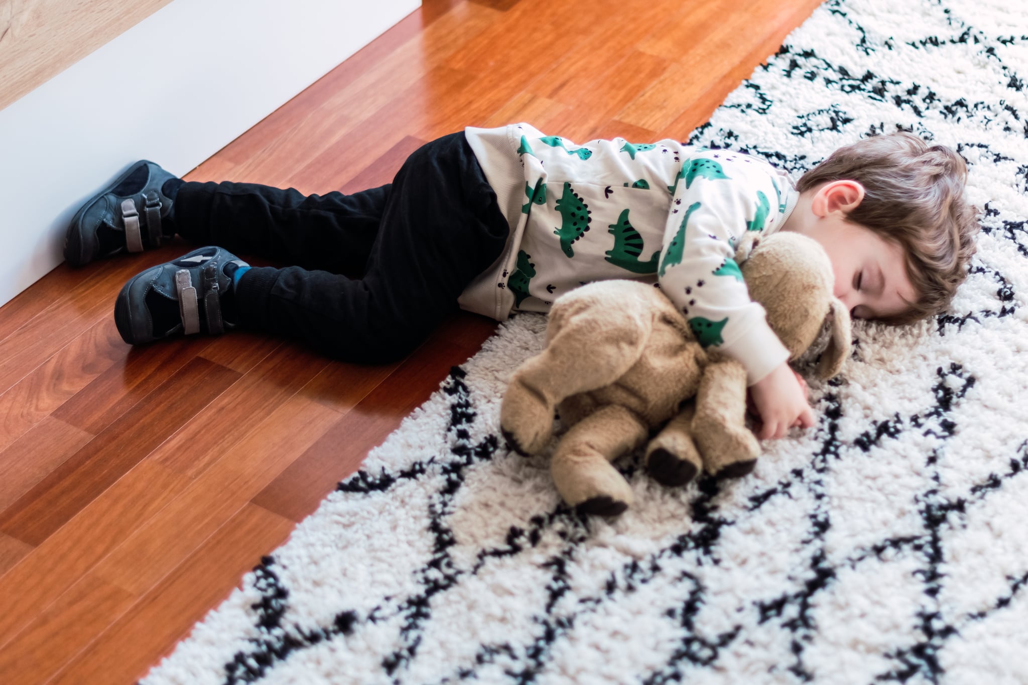 Child sleeps on the floor and hugs his stuffed dog.