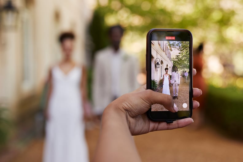 woman holding smartphone while photographing bride and groom