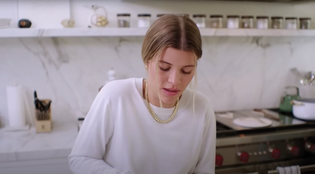 The kitchen is covered with white granite, from the countertops and shelving to the backsplash. The spice jars are all labeled and matching for a cohesive look, and she has Caraway cookware in white and green.