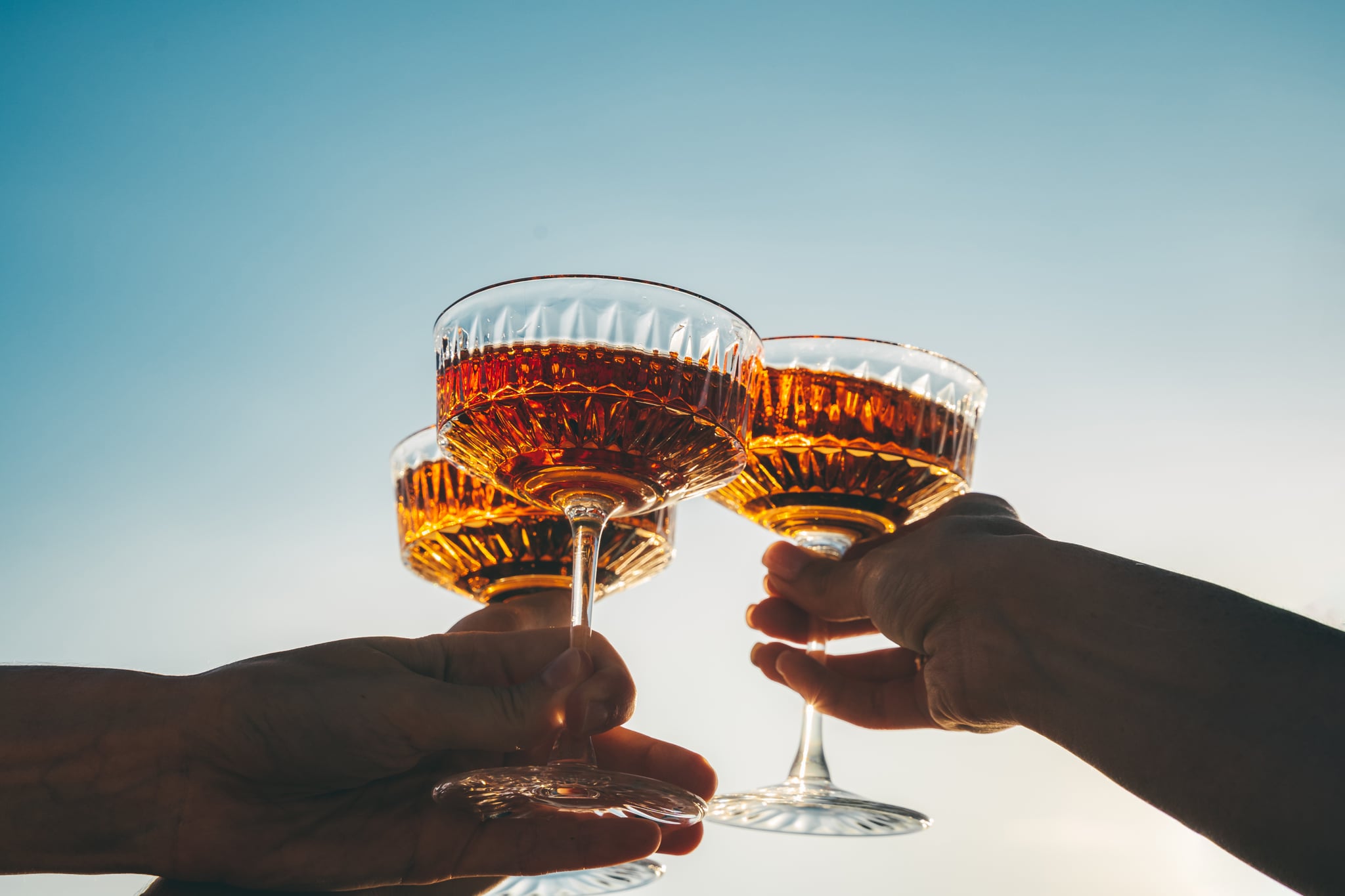 A close-up shot of friends clinking orange wine glasses at sunset.