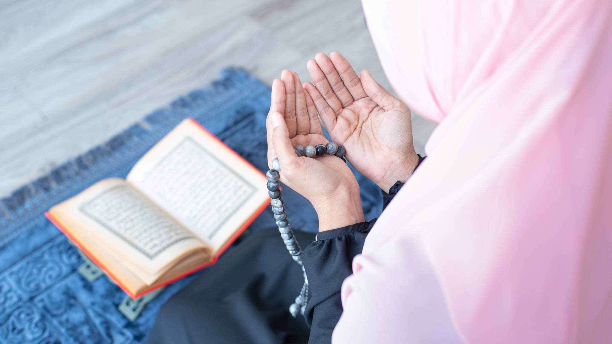 side of asian young beautiful muslim woman pray with beads and read quran sit on carpet mat with meditation in mosque.