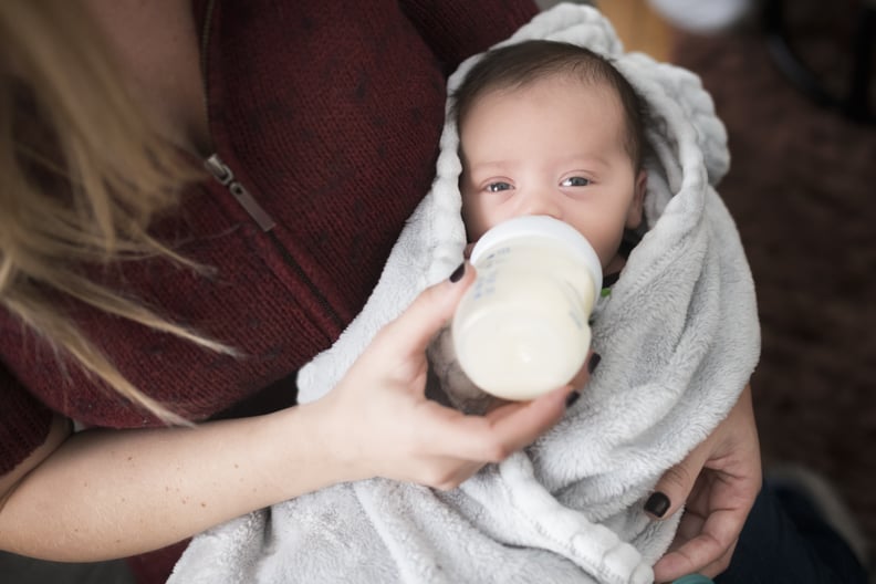 Newborn baby is fed by mother through a bottle at home.