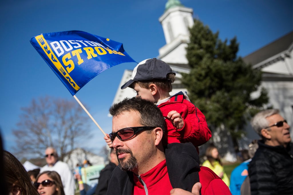 A little boy sat on his father's shoulders holding a "Boston strong" flag.