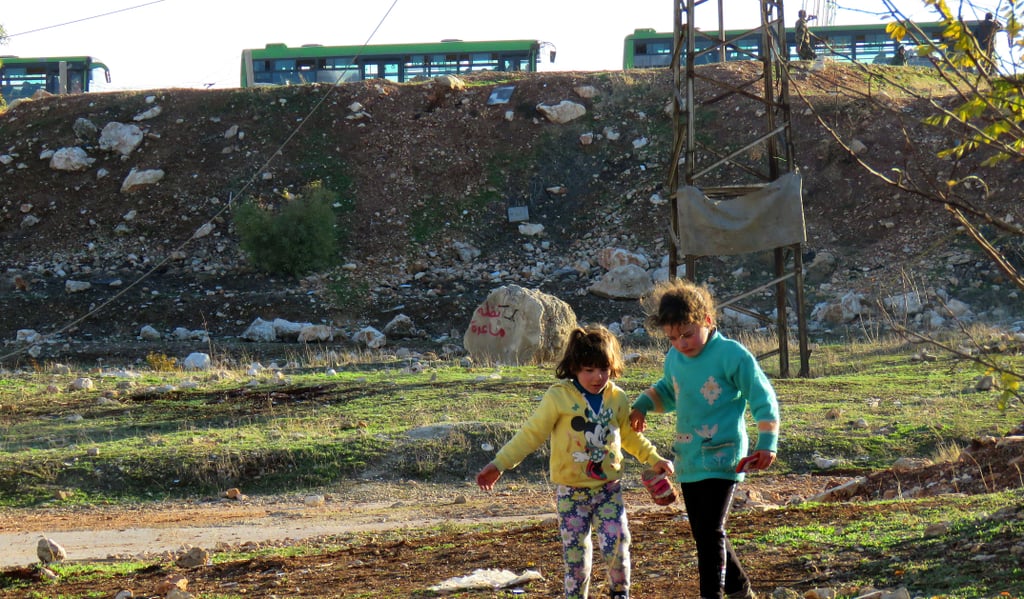 Children walk among the rubble as the evacuation takes place behind them in Aleppo on Dec. 15.