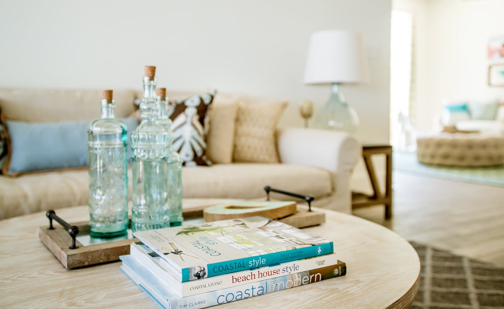 Decorative glass bottles, a rustic tray, wood pops, and a stack of gulf-coast-focused books create the perfect beach house coffee table.