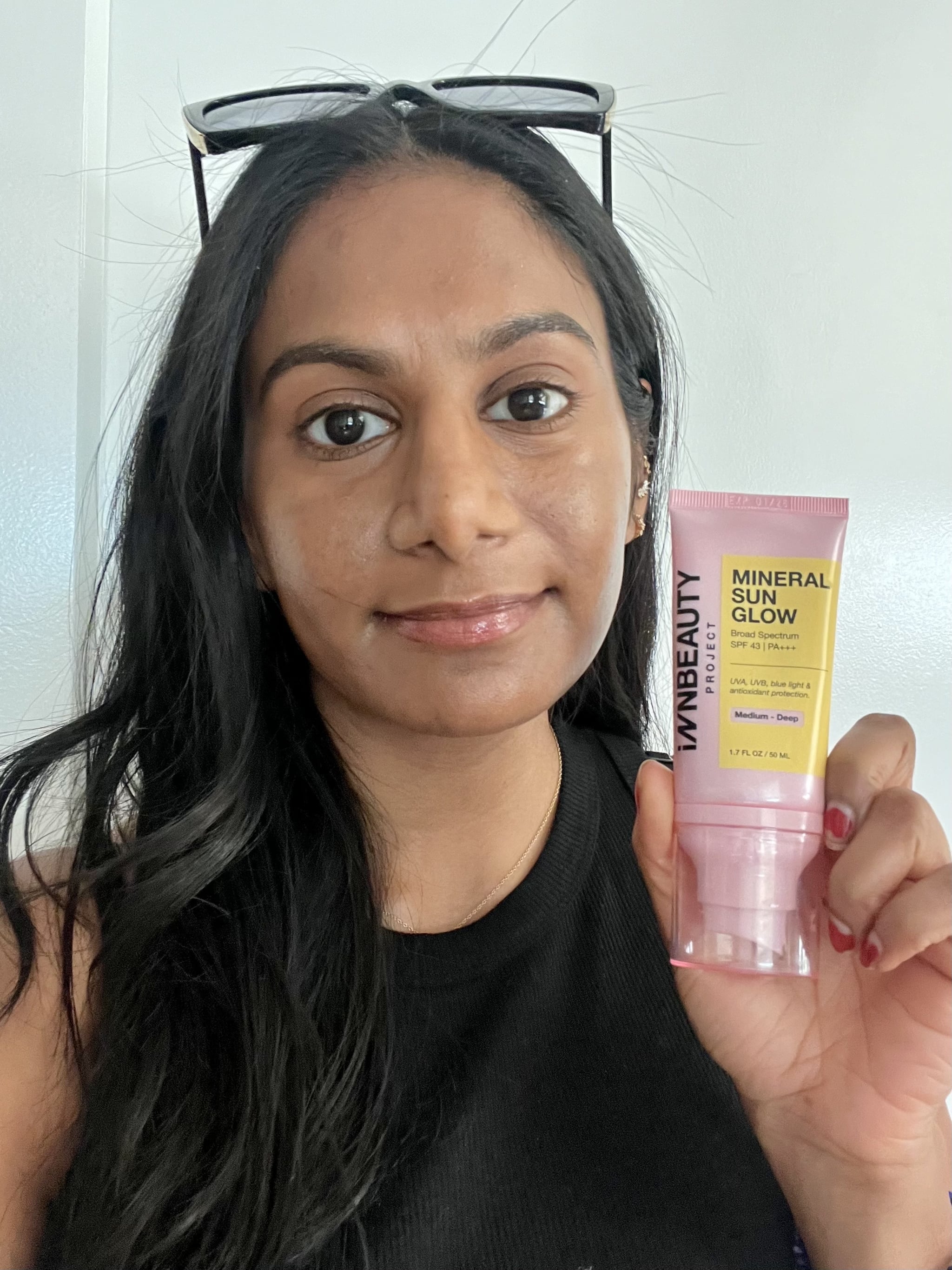 Woman wearing the Innbeauty Project Mineral Sun Glow Sunscreen and holding it in her hand.