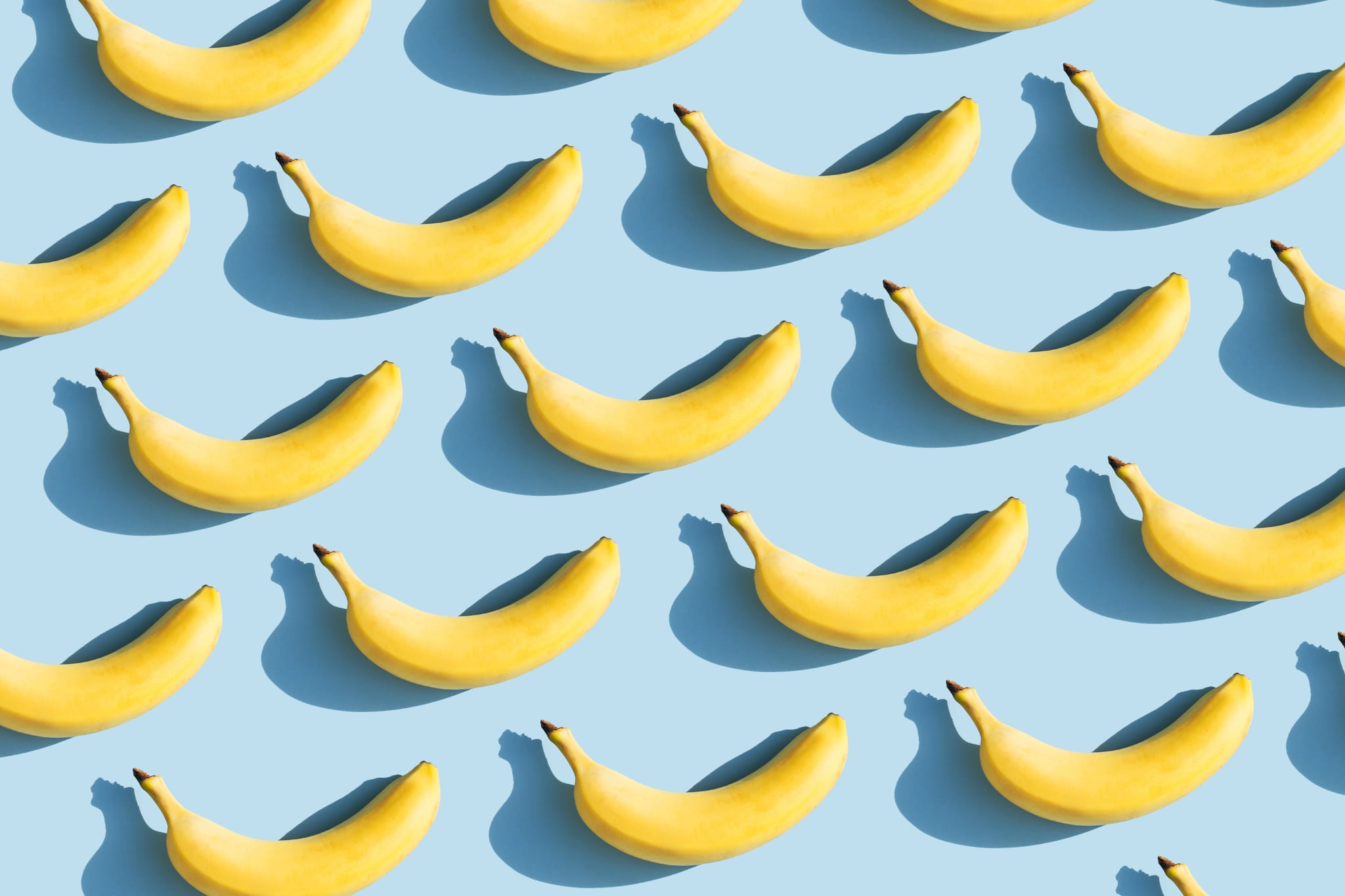 Colourful fruit pattern of fresh yellow bananas on blue background with shadows. Fruit concept. Flat lay, top view.