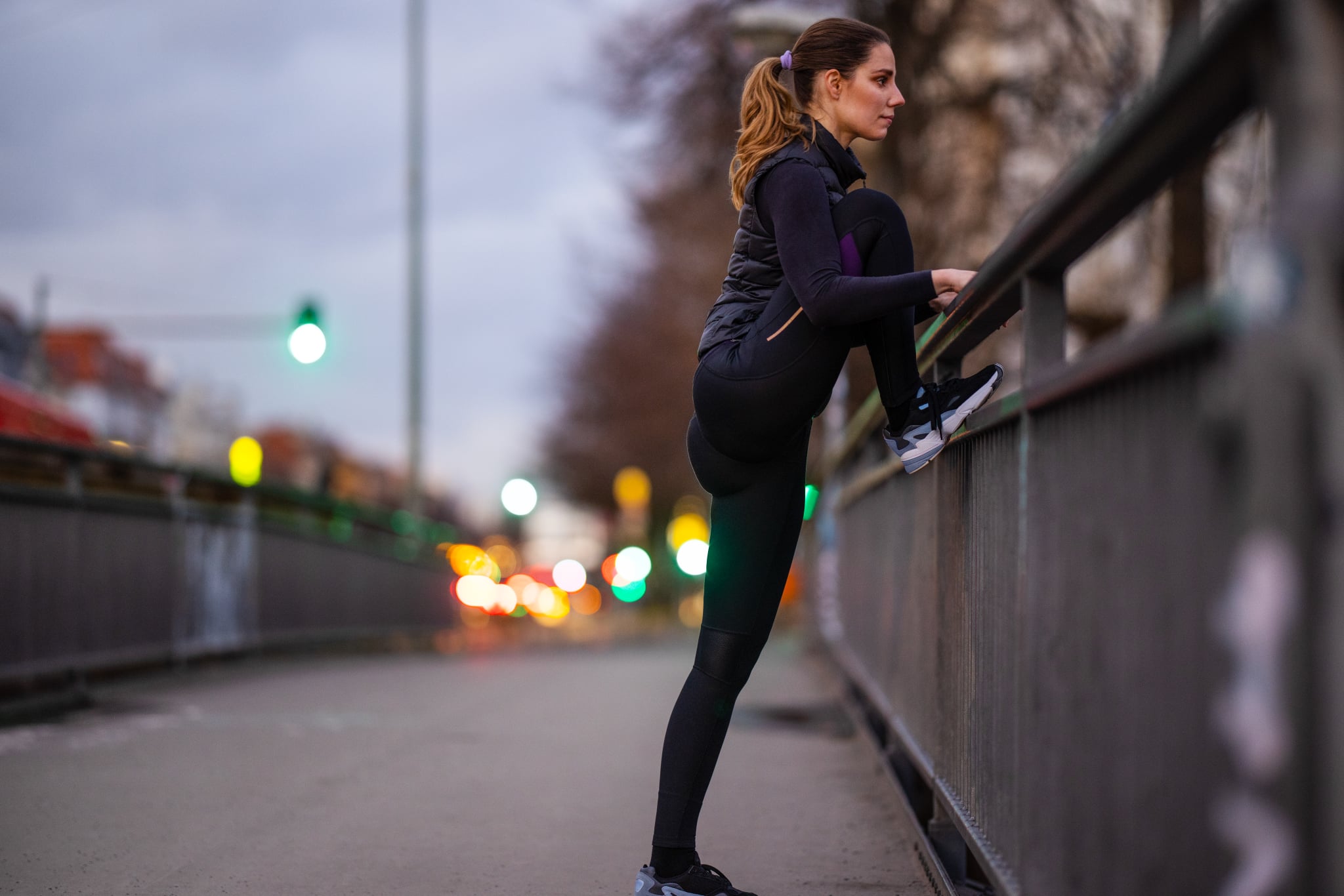 Fitness woman exercising on the sidewalk. Female in sportswear stretching legs in city in the evening.