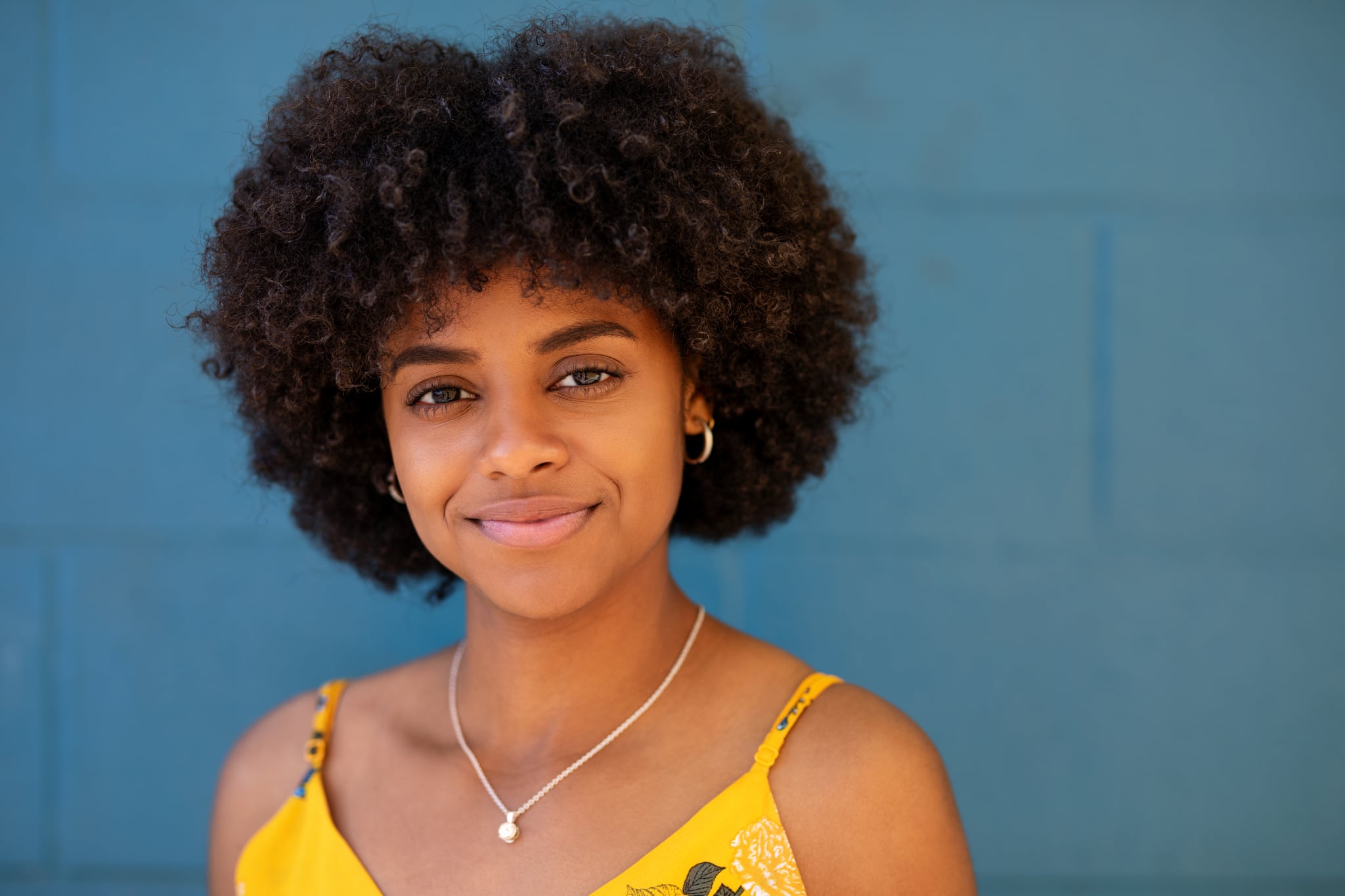 Close-up of a beautiful woman standing against blue wall. Woman with curly hair looking at camera.