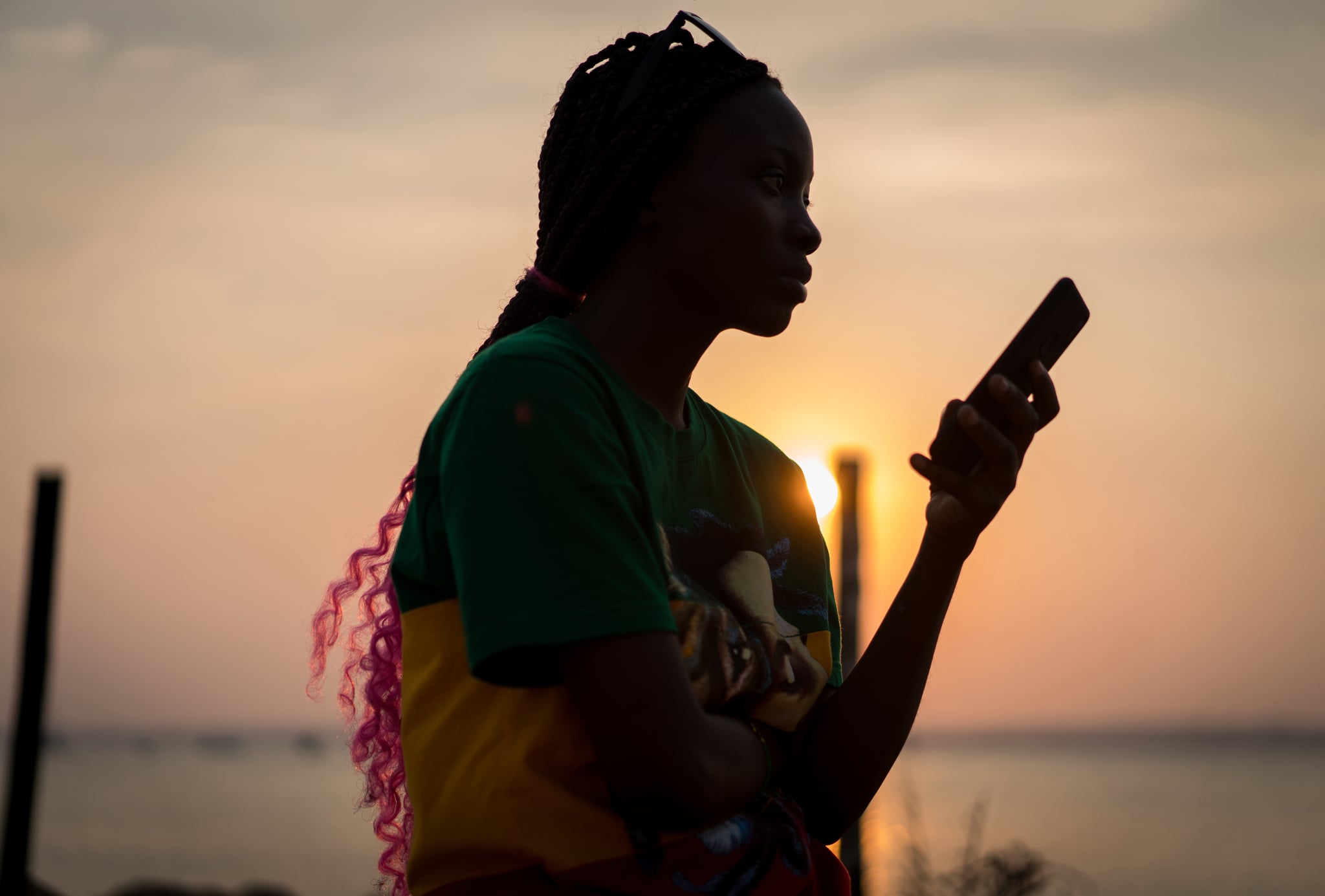 Afro american woman sitting on shore using a mobile phone at sunset